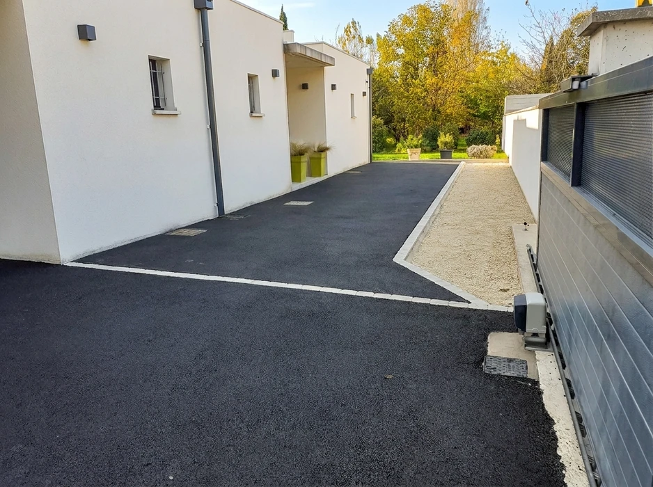 Allée de maison individuelle avec enrobé bitumineux noir fraîchement posé, délimitée par des bordures blanches