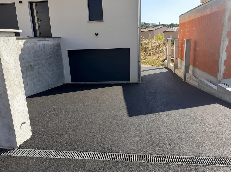 Allée de garage en enrobé bitumineux noir fraîchement posé, accès à un garage semi-enterré avec porte sectionnelle noire