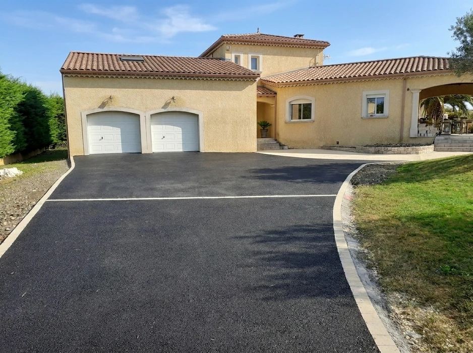 Allée de maison rénovée en enrobé bitumineux noir, bordée de pavés en pierre calcaire beige