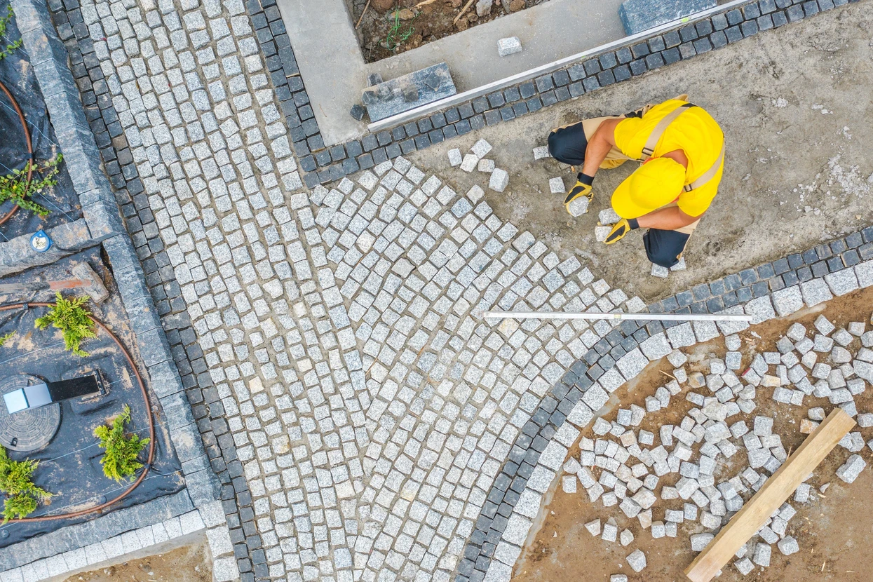 Chantier extérieur de pavage avec ouvrier en combinaison jaune haute visibilité posant des pavés de granit
