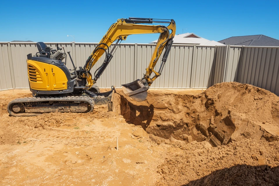 Chantier de terrassement en extérieur avec mini-pelle hydraulique jaune sur chenilles caoutchouc excavant du sable et terre
