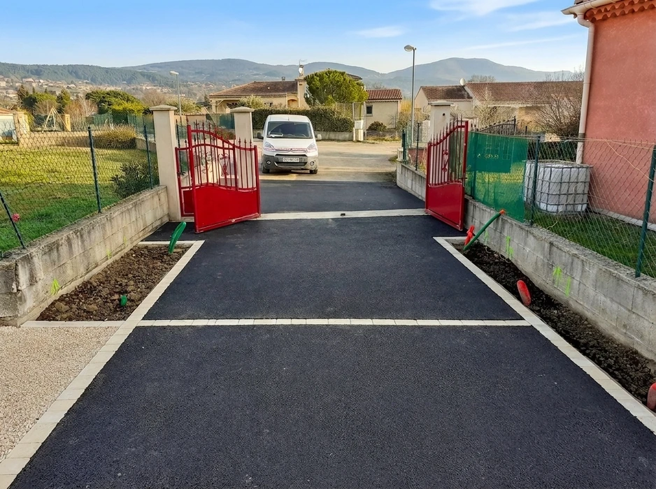 Entrée de propriété rénovée avec allée en enrobé bitumineux noir, bordures en pavés béton blancs, portail battant rouge en fer forgé