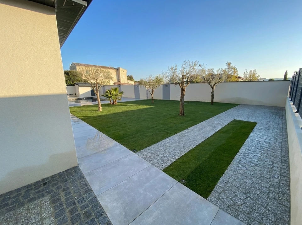 Allée de maison fraîchement enrobée en béton bitumineux noir, avec une bande de délimitation en pavés de béton blanc